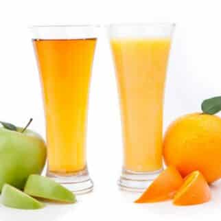 Two tall glasses, one of orange juice and one of apple juice.