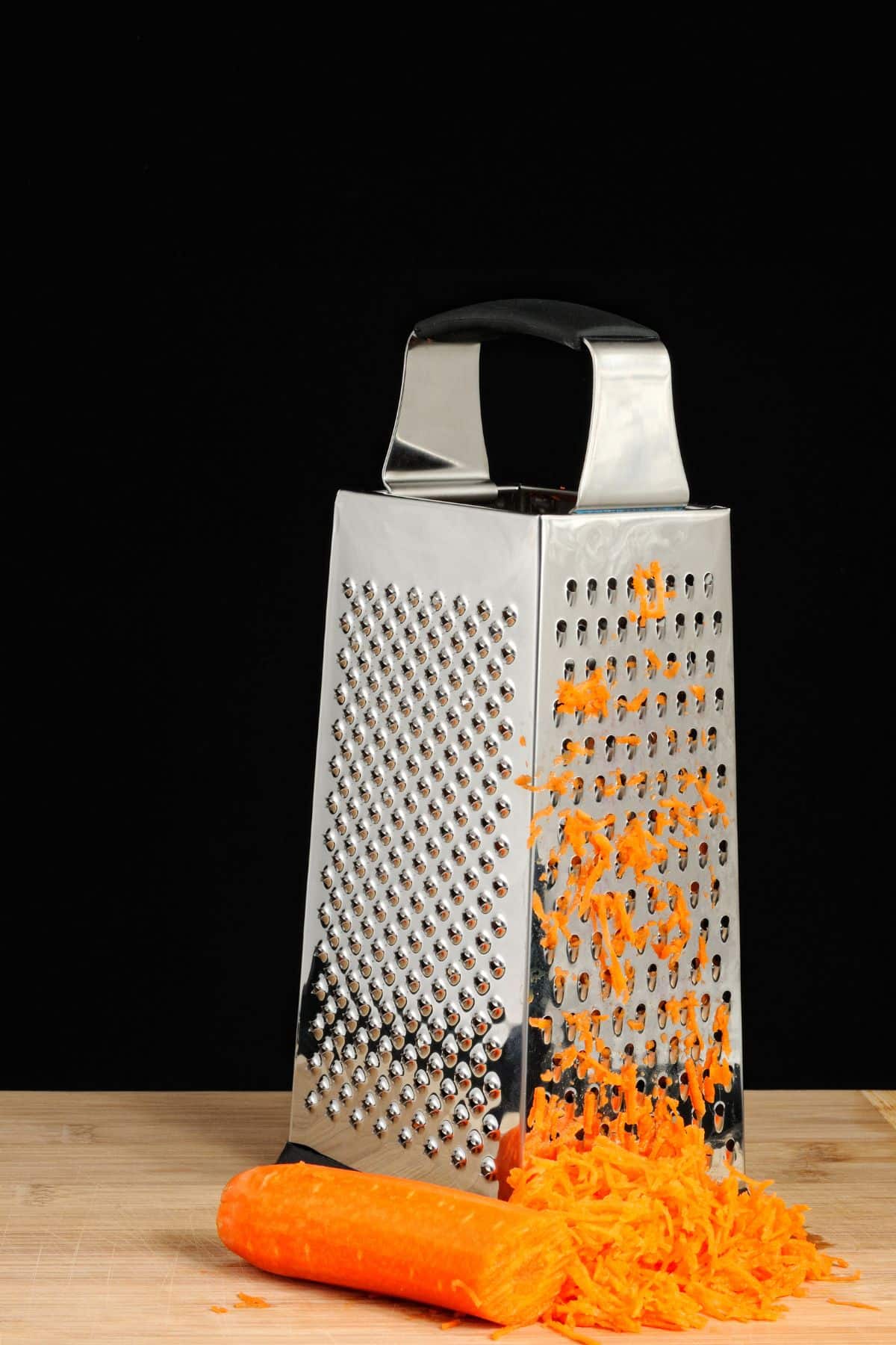 A box grater with a carrot half shredded.