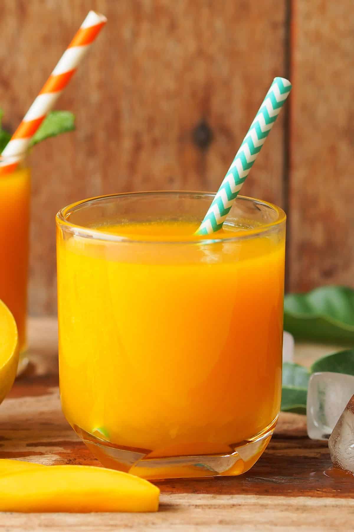 A short glass of mango carrot juice with a striped straw.