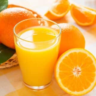 A glass of freshly squeezed orange juice next to fresh whole oranges.
