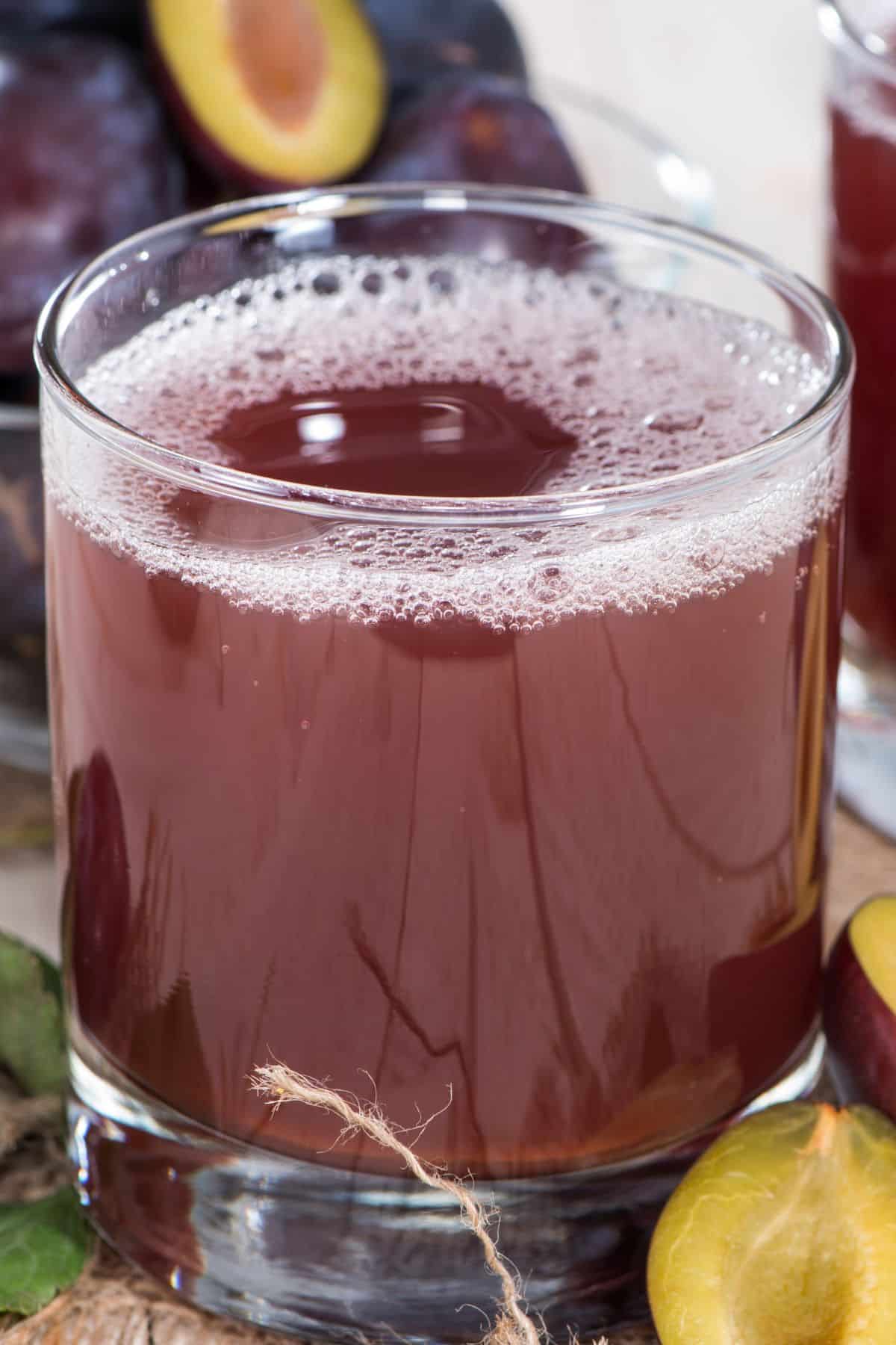 A short glass of plum juice with whole plums on a table.