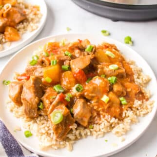 A white dinner plate of brown rice topped with sweet and sour pork.