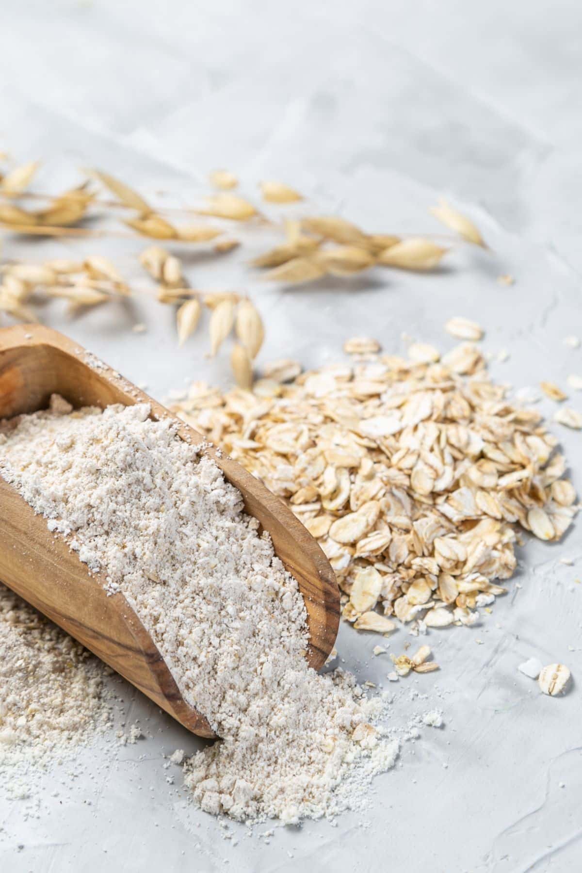 Oats on a counter next to a scoop of fresh ground oat flour.