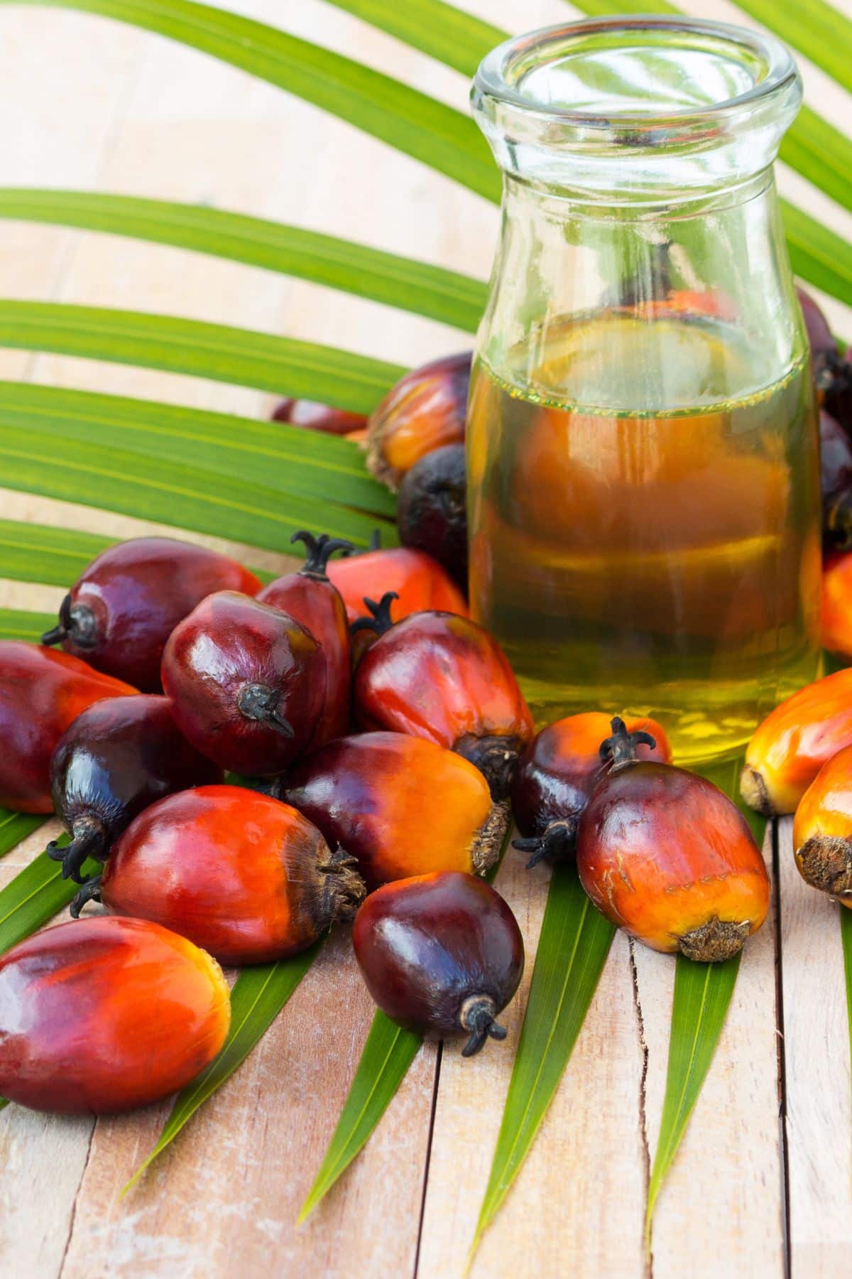 a jar of palm oil behind palm fruit on a wooden table.