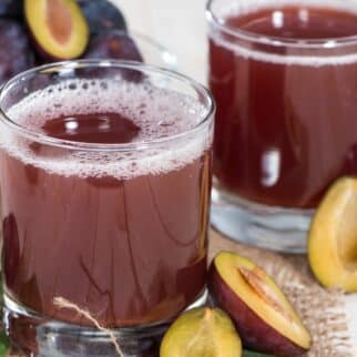 Two short glasses of fresh plum juice with halved plums on a table.
