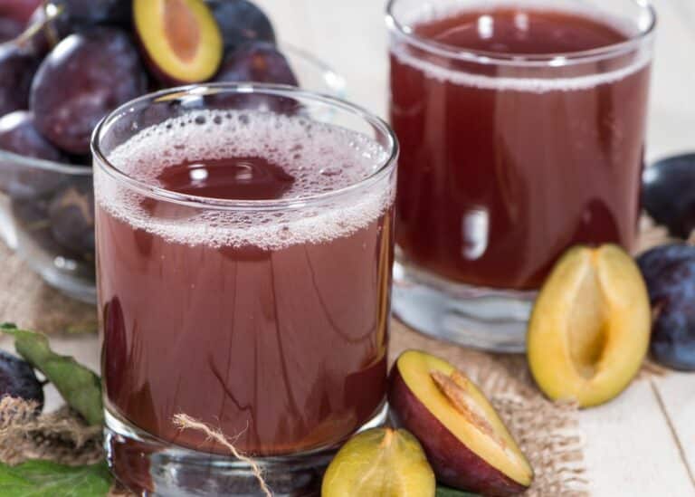 Two short glasses of fresh plum juice with halved plums on a table.
