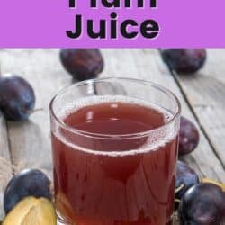 A short glass of plum juice with whole plums on a table.