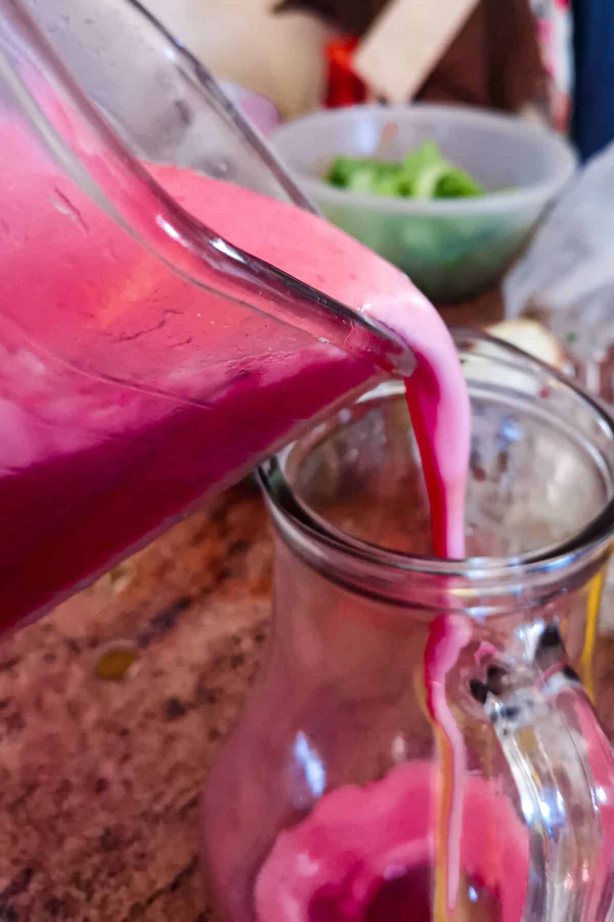 Blender jar pouring raspberry juice into a pitcher.