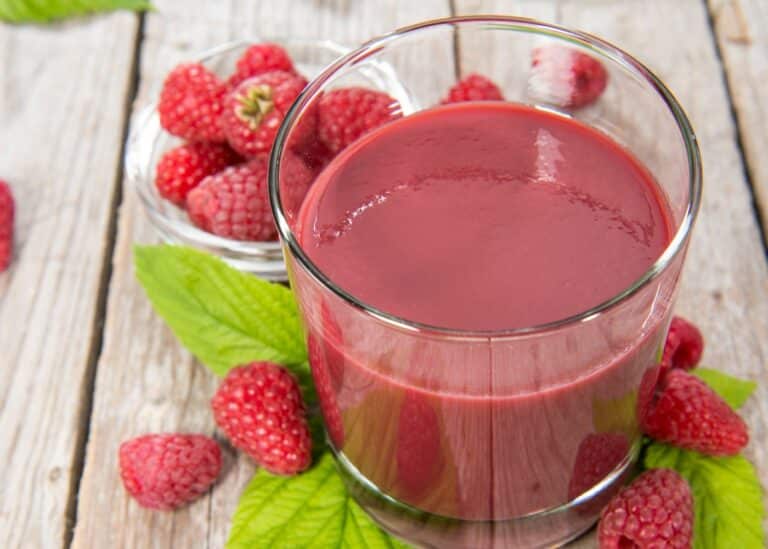 A glass of raspberry juice on a wooden table.