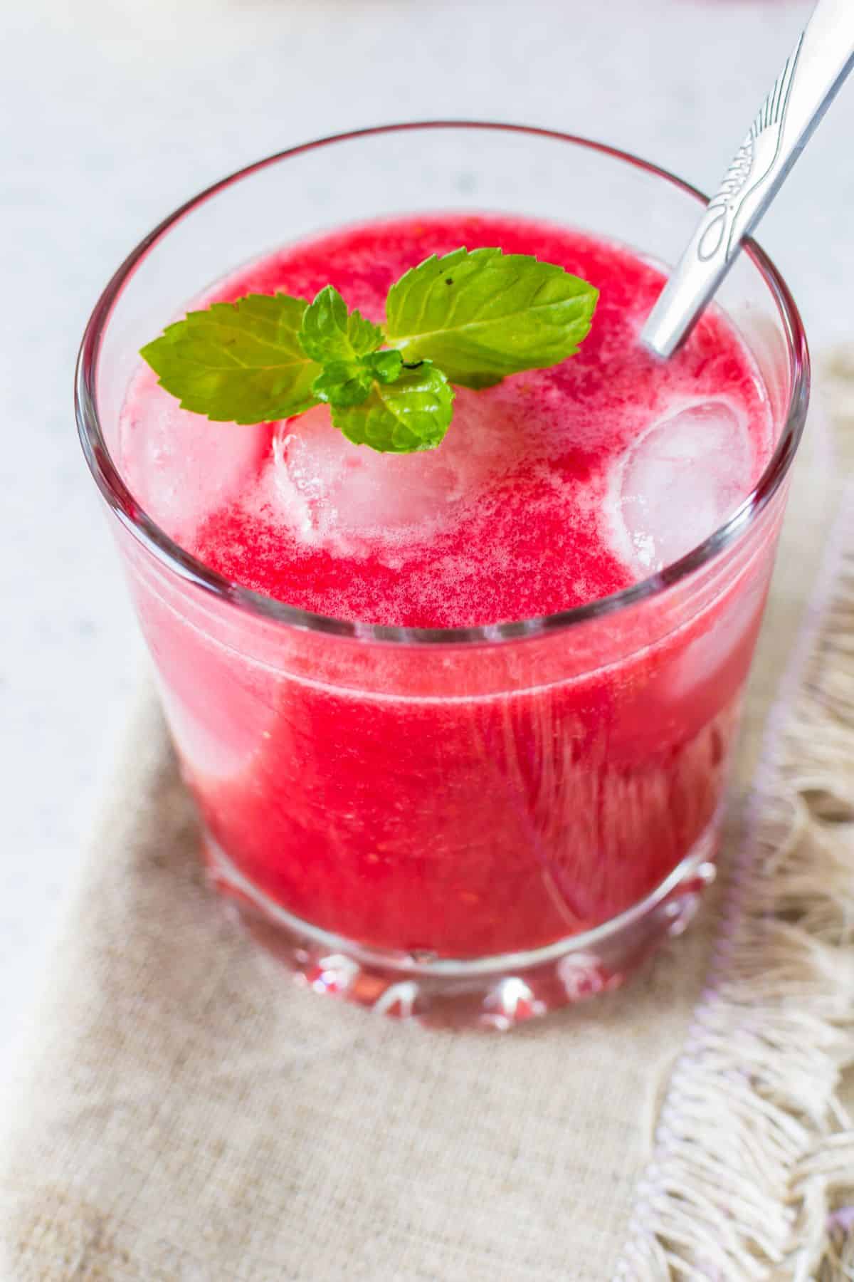 A short glass of raspberry mint juice with a silver spoon.