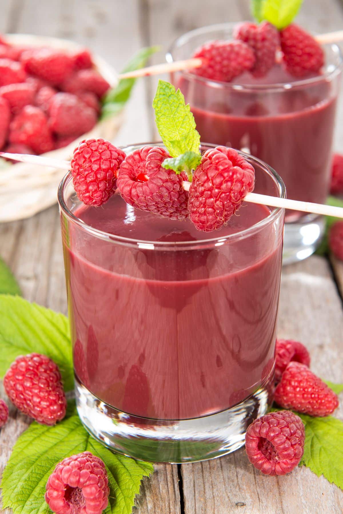 A skewer of raspberries across a glass of fresh raspberry juice.