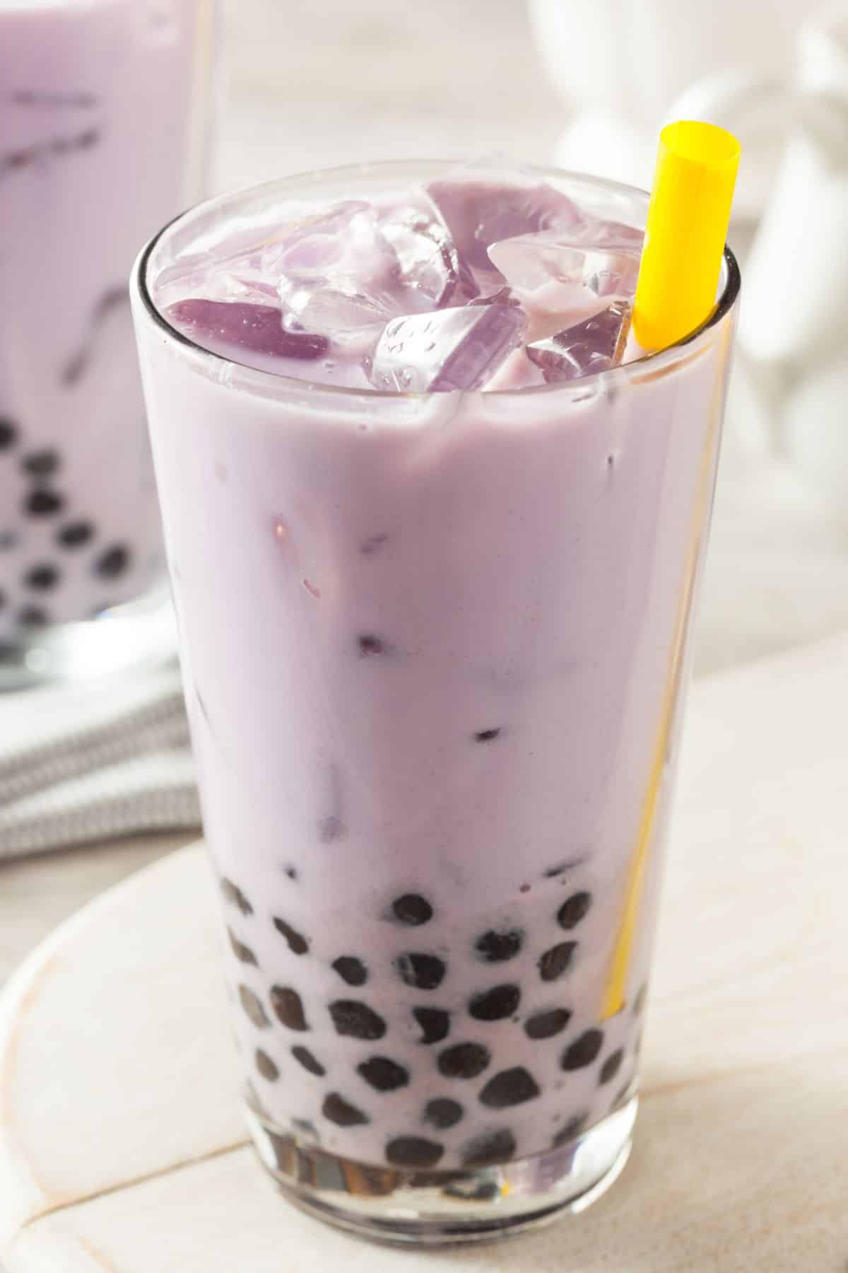 Taro milk tea in a glass with boba pearls and a straw.