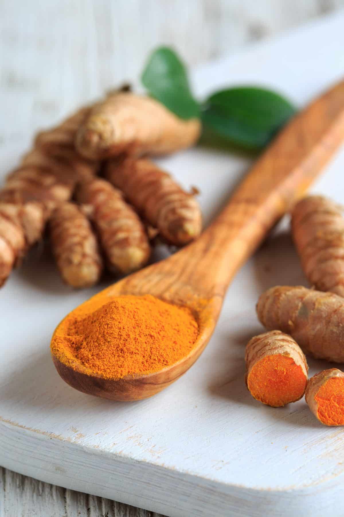 ground turmeric on a wooden spoon, surrounded by raw turmeric.