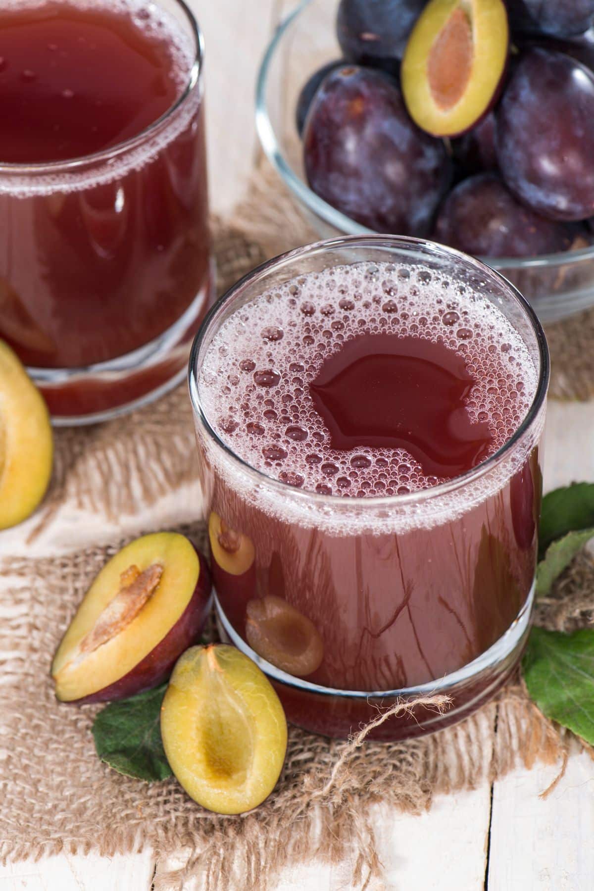 Two glasses of plum juice on a table with fresh plums.