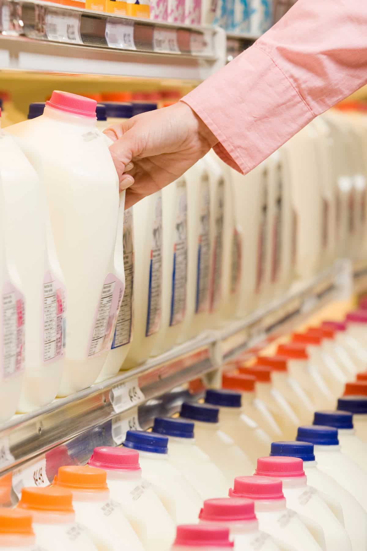 woman grabbing a carton of milk off shelf at grocery store.