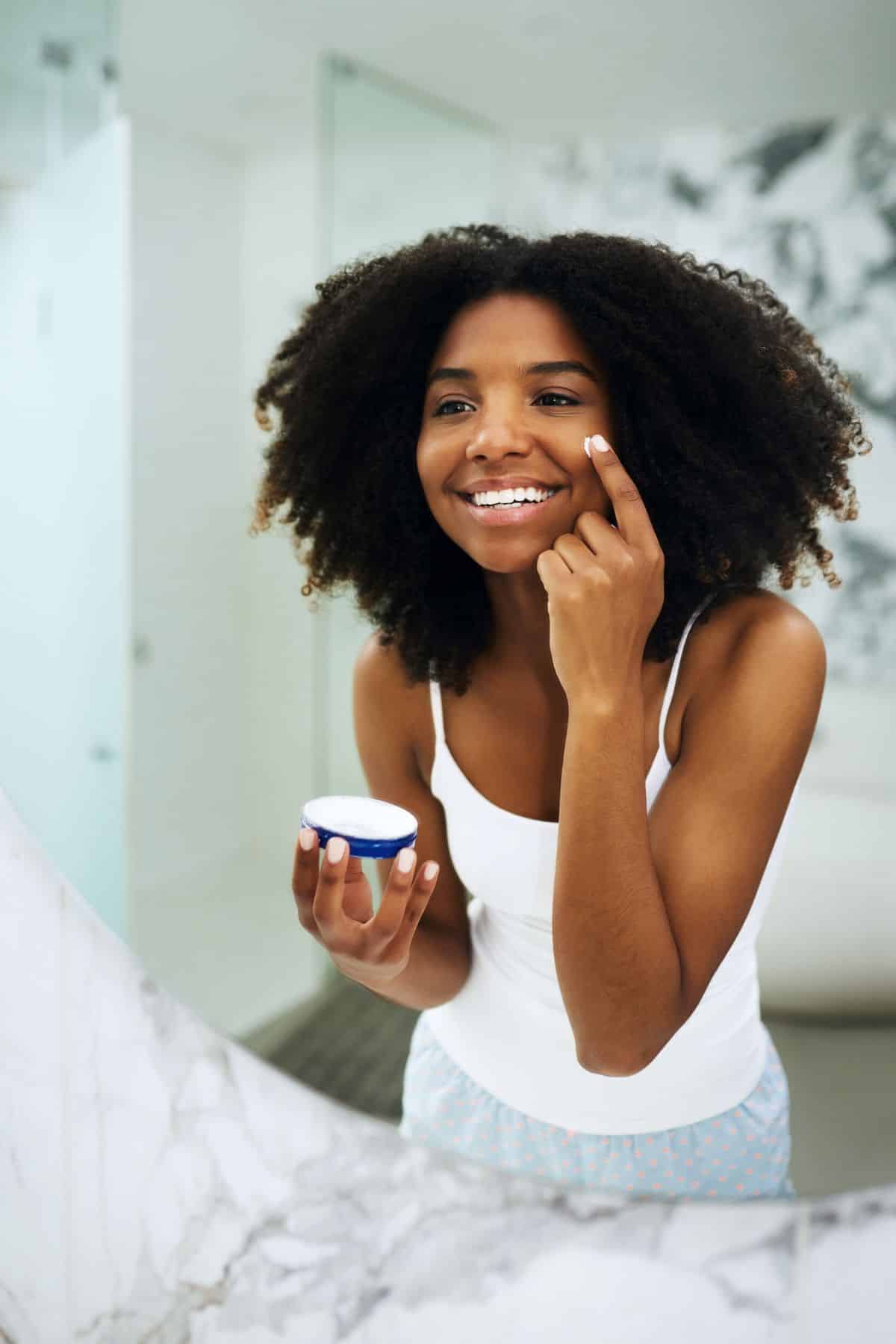 young woman putting cream on her face.