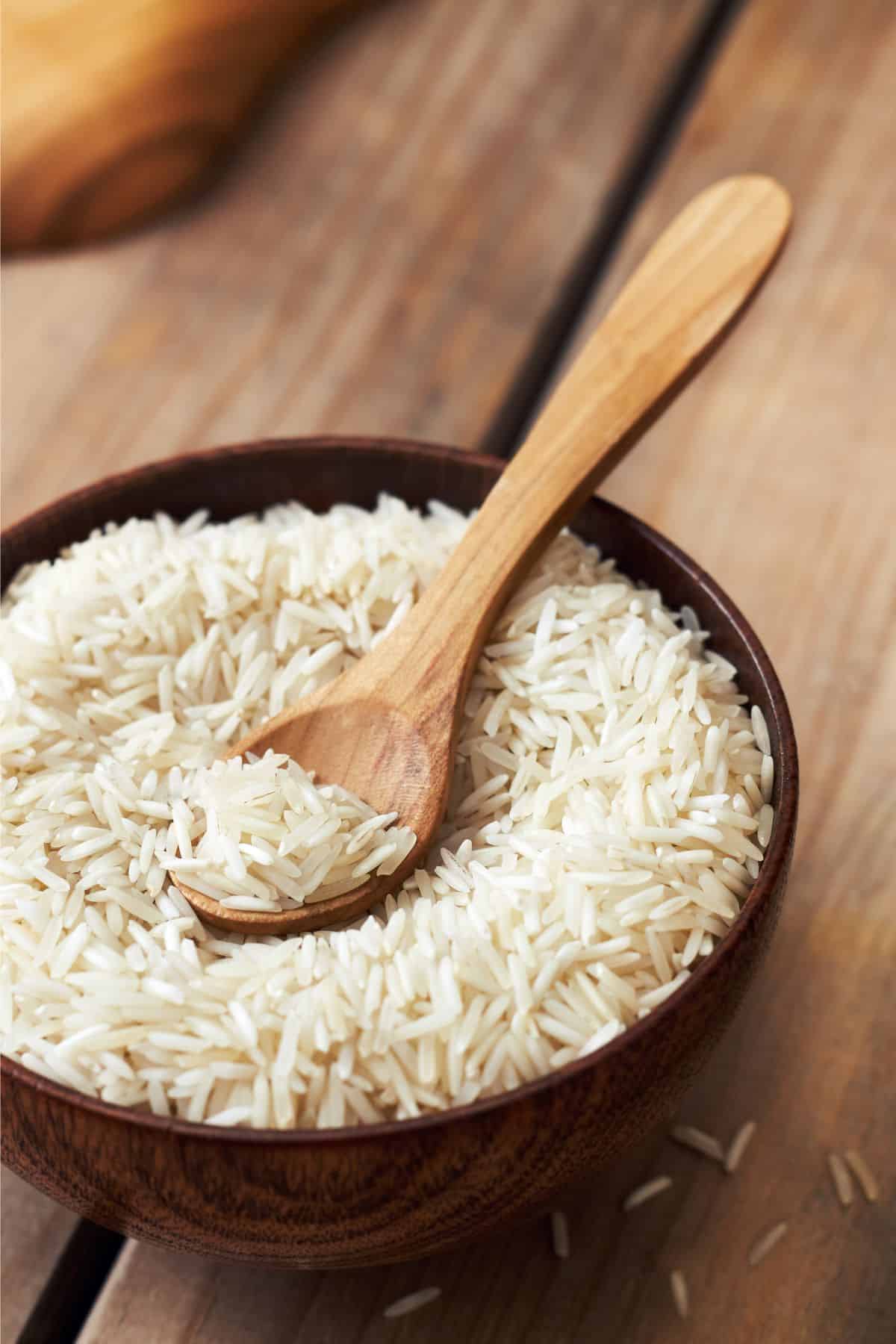 a wooden bowl of basmati rice with a wooden spoon.