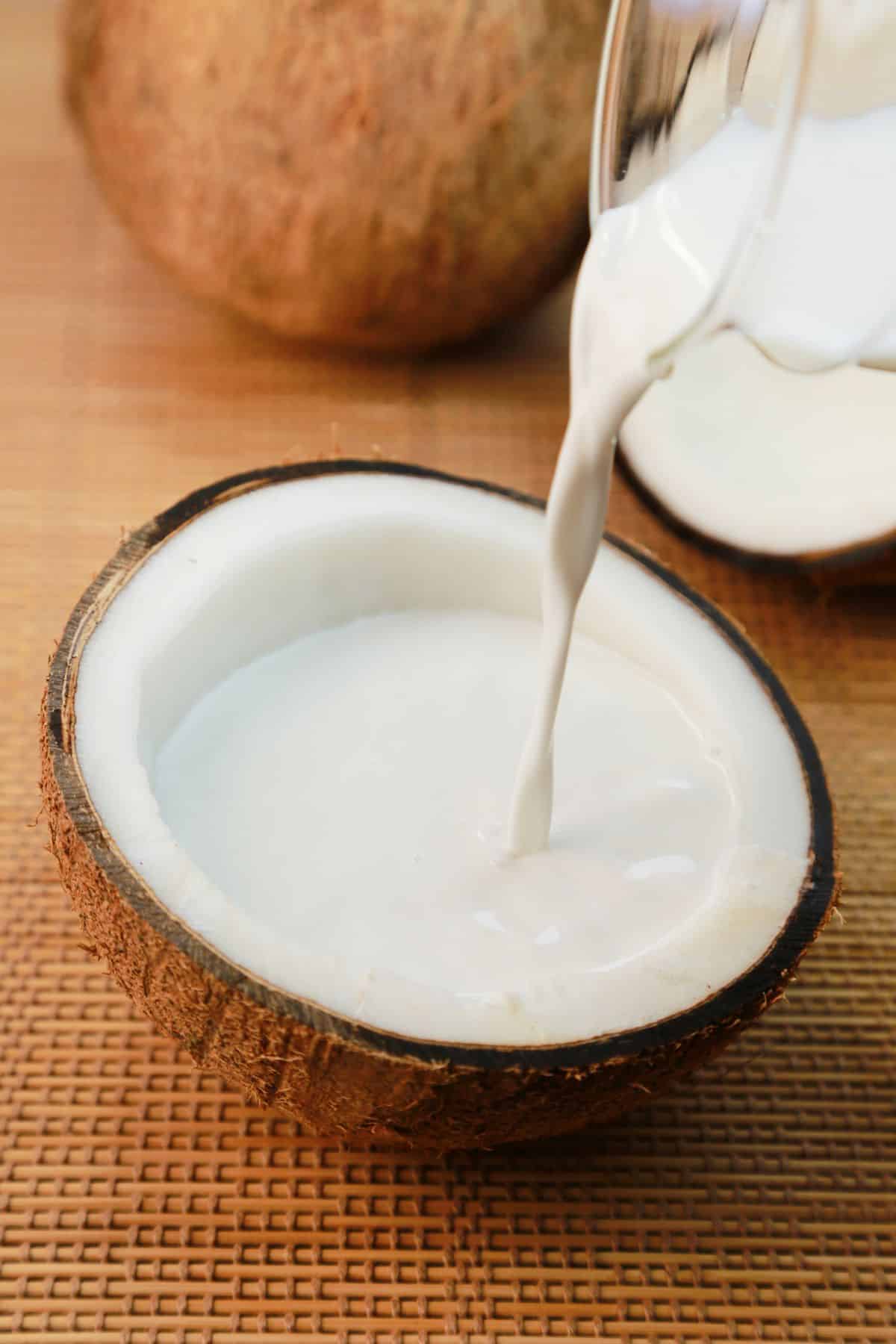 coconut milk being poured into half of a coconut.