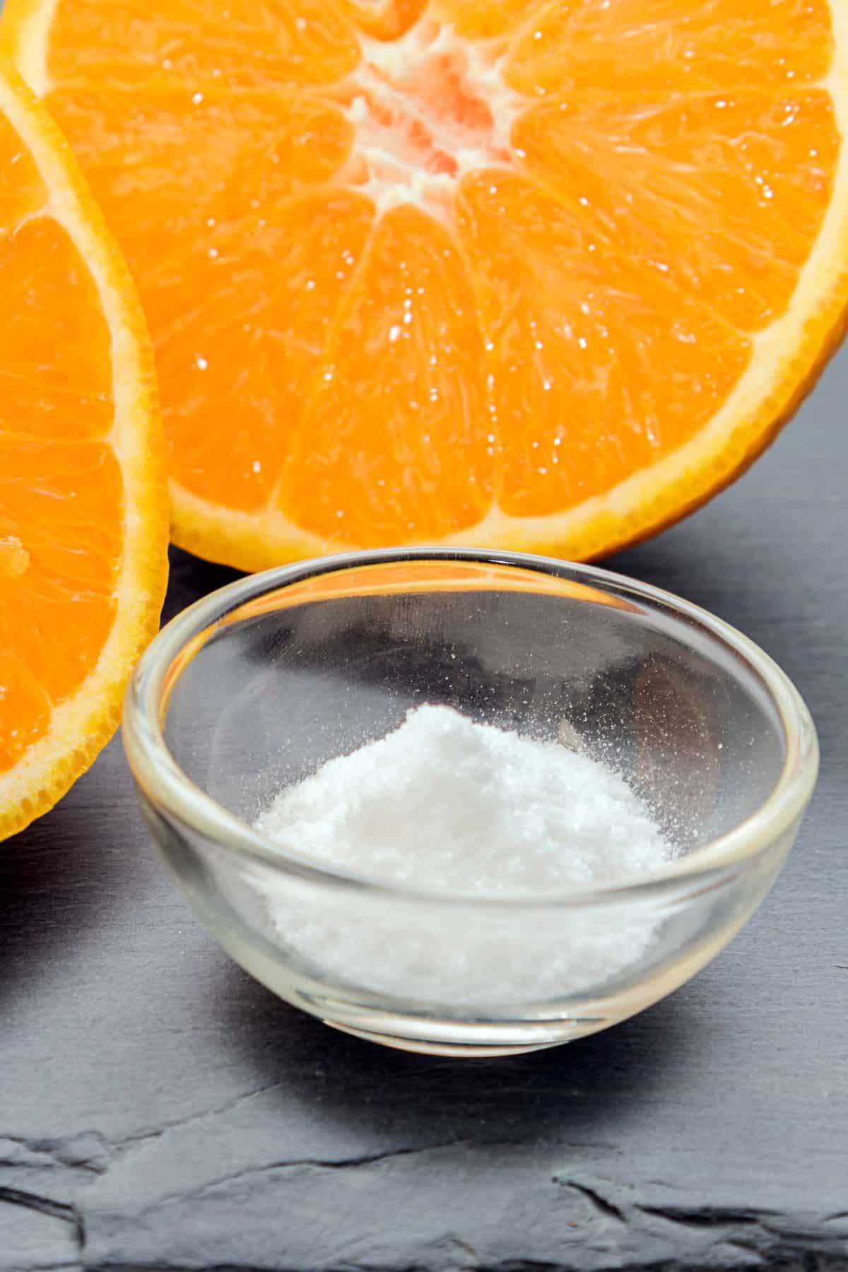 a bowl of ascorbic acid next to a sliced orange.