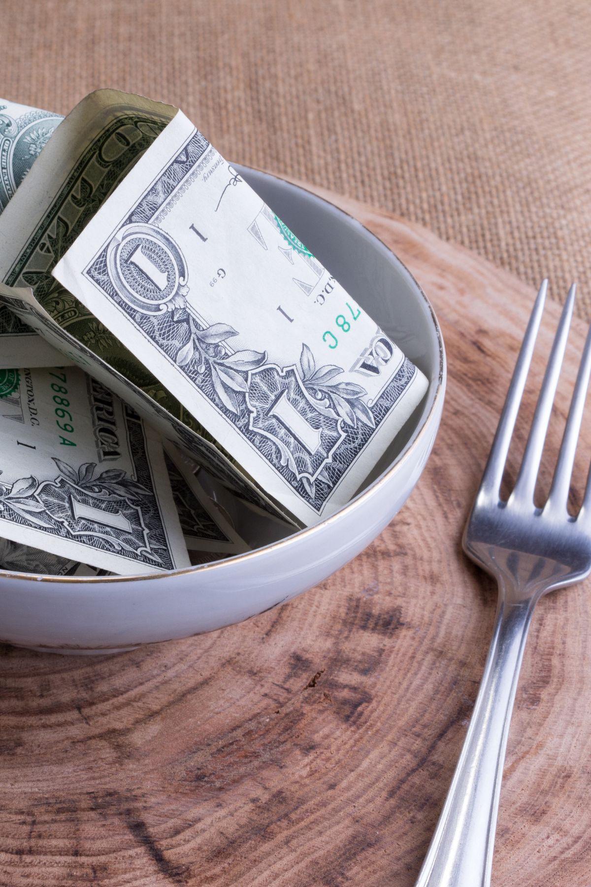a bowl of one dollar bills beside a fork.
