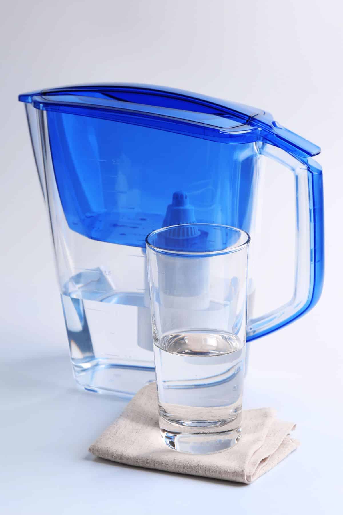 a water filter pitcher behind a glass of water.