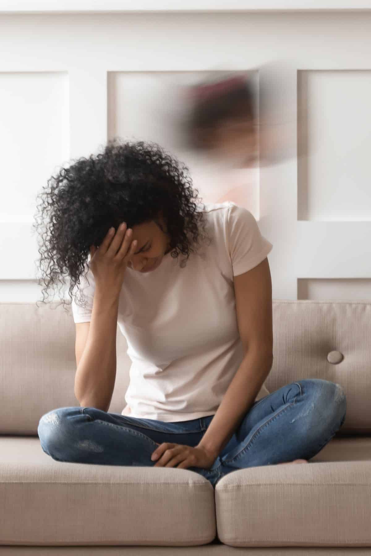 a tired woman on a couch holding her hand in her hands.