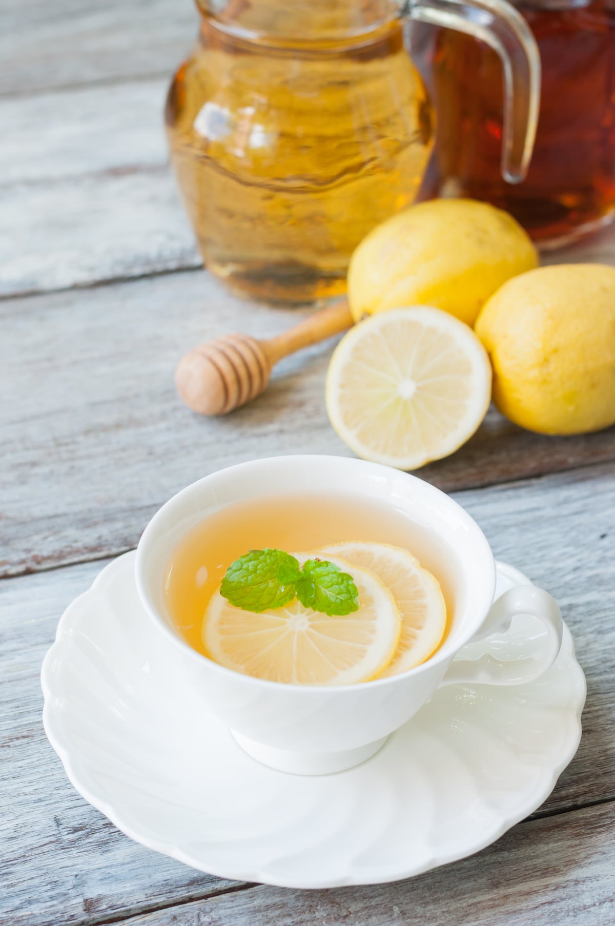 lemon honey tea in a white mug with lemons and honey in background.