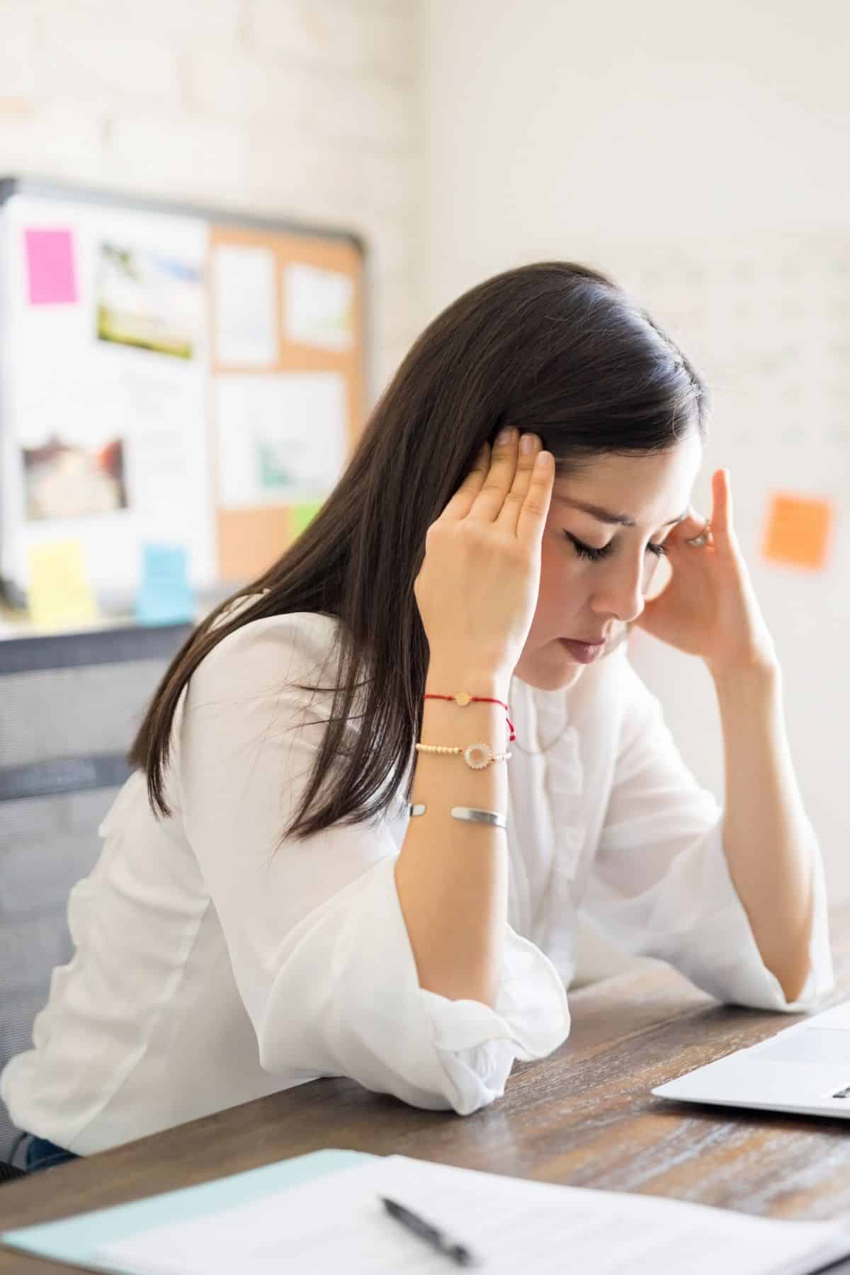 a woman sitting at her desk holding her head.