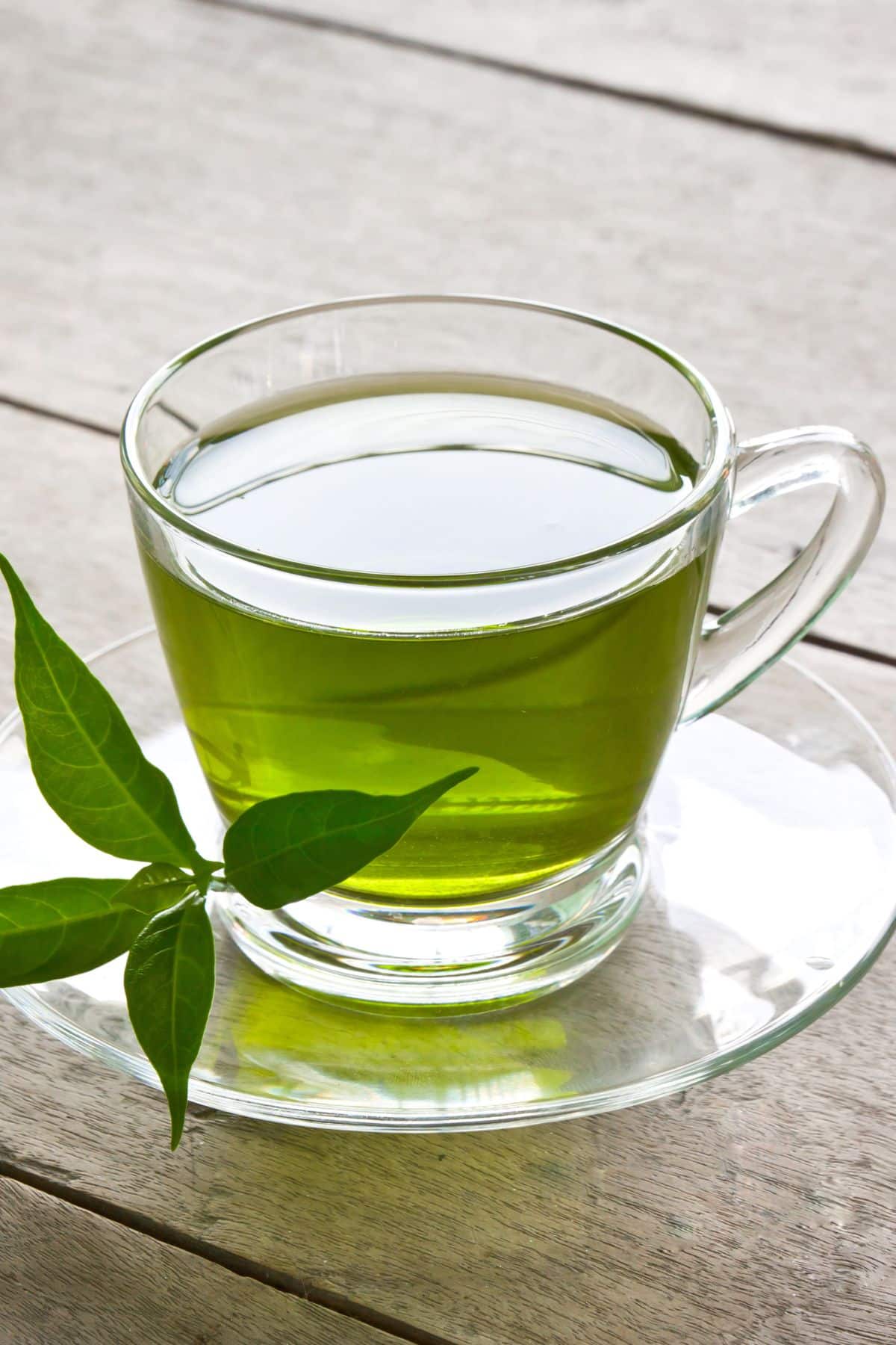 a clear mug of green tea on a wooden table.