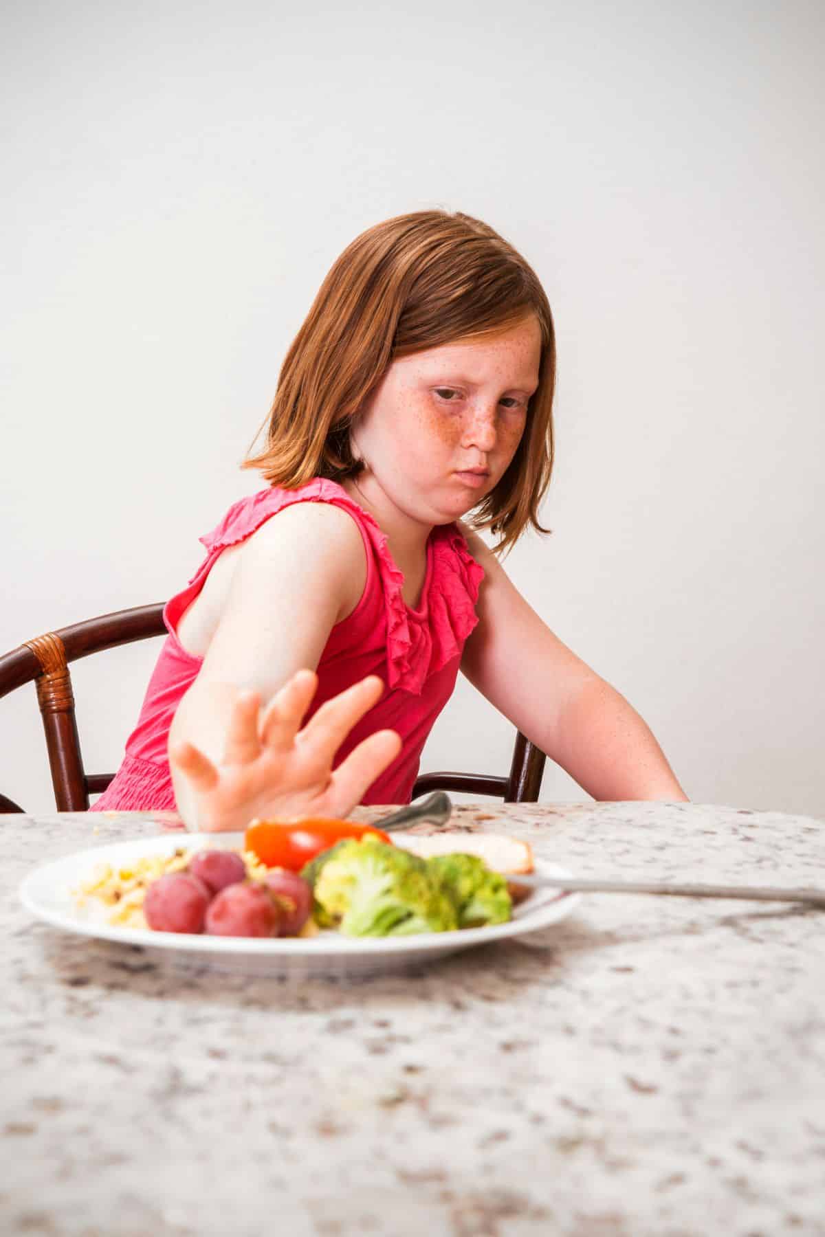a child pushing away a plate of healthy foods.