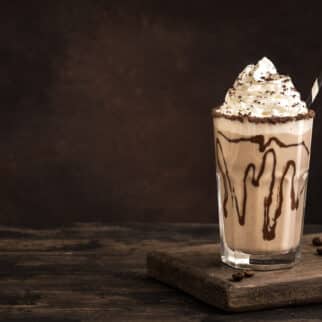 a dairy-free iced mocha topped with whipped cream in a glass with chocolate syrup.