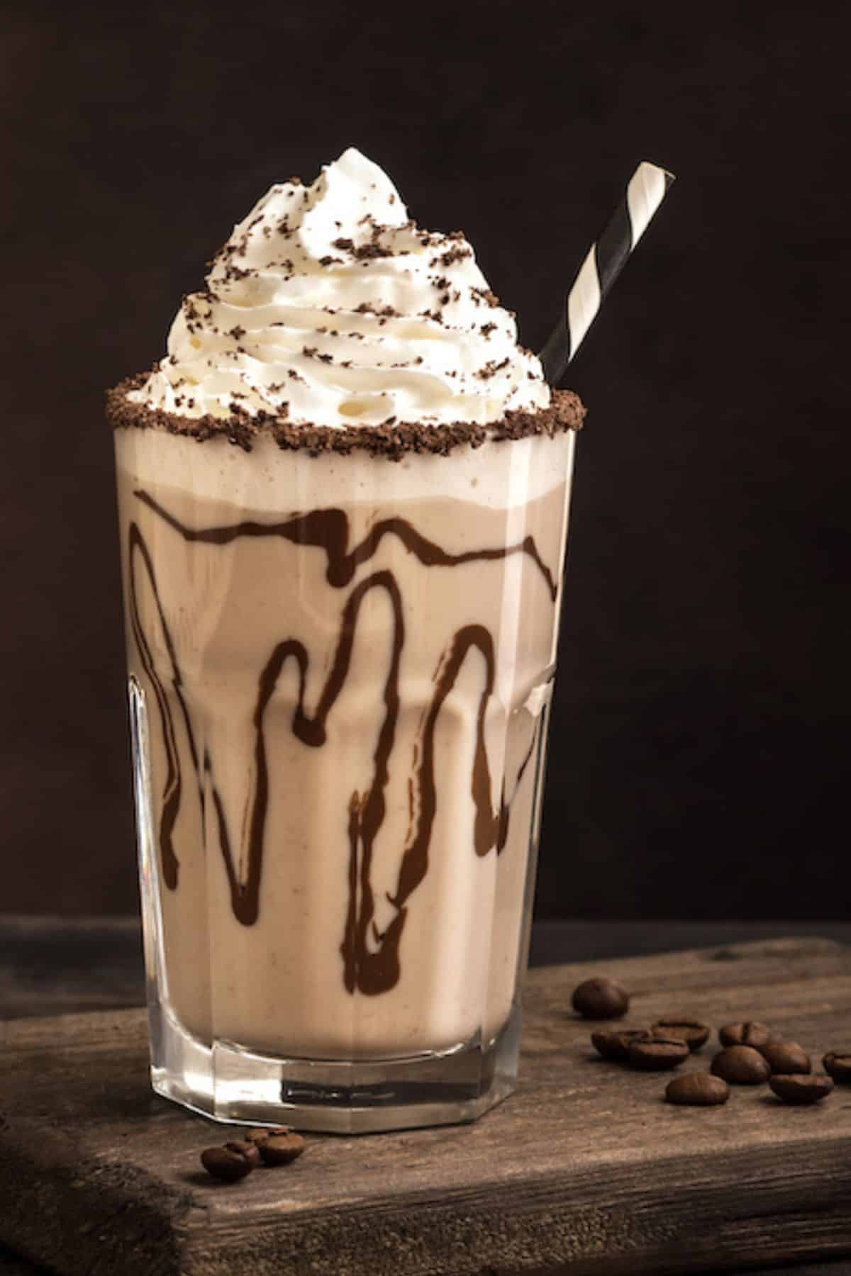 a dairy-free iced mocha topped with whipped cream in a glass with chocolate syrup.