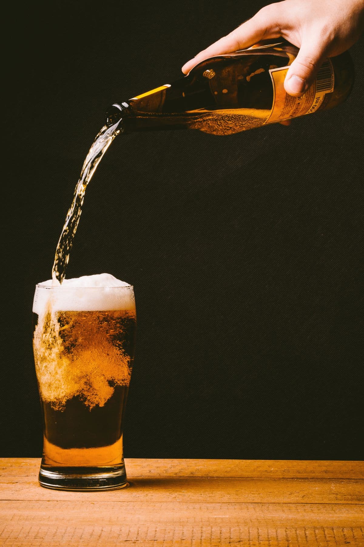 a person holding a bottle of beer, pouring it into a glass.