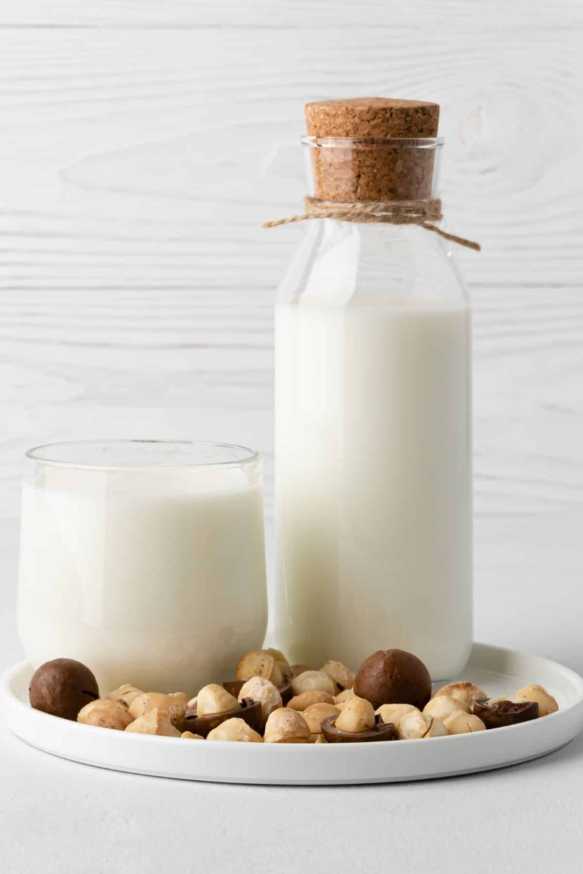 macadamia milk in a jar and glass on a tray filled with macadamia nuts.