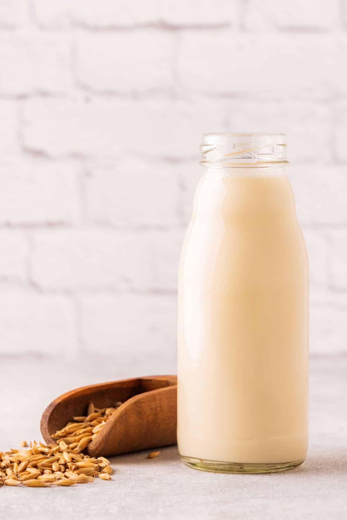 a glass of oat milk beside a scoop of oats.