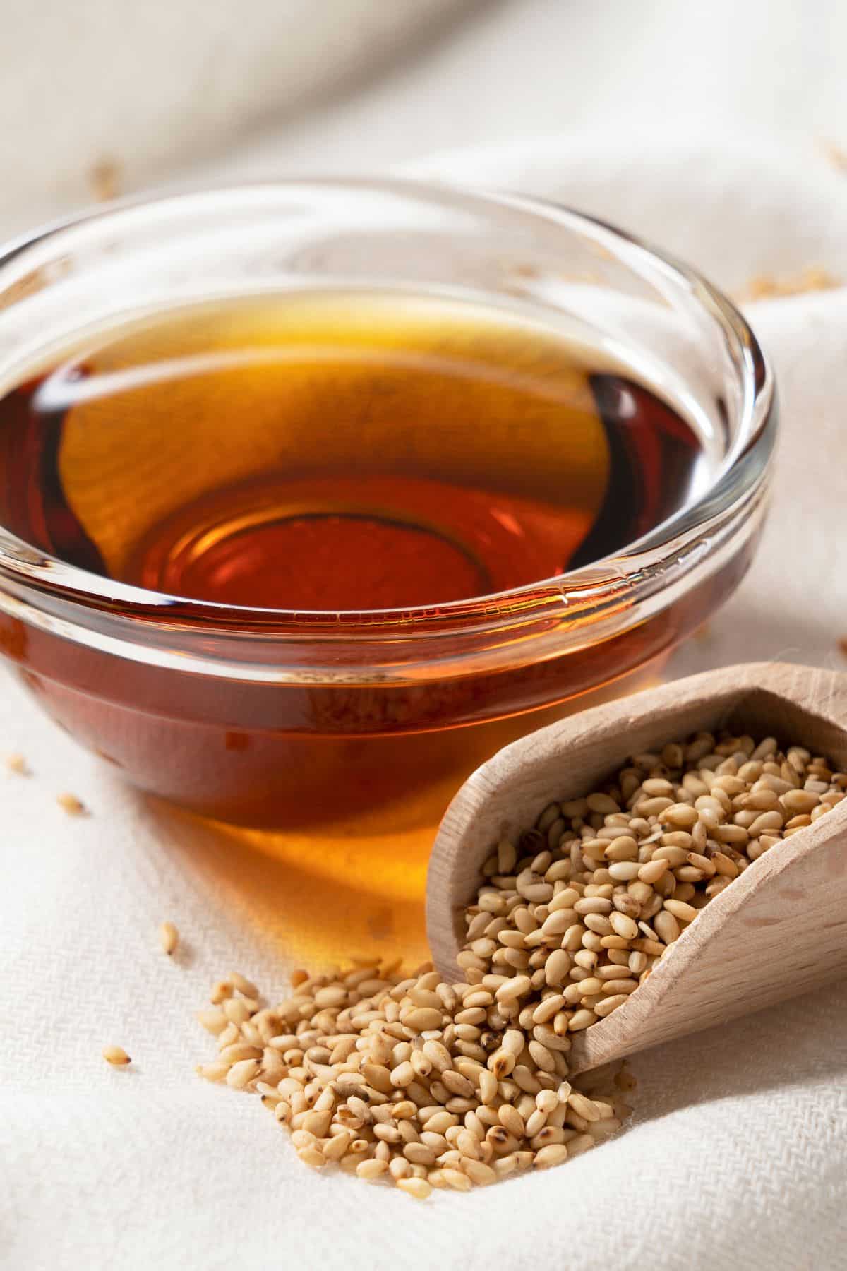 a bowl of sesame oil beside a scoop of sesame seeds.