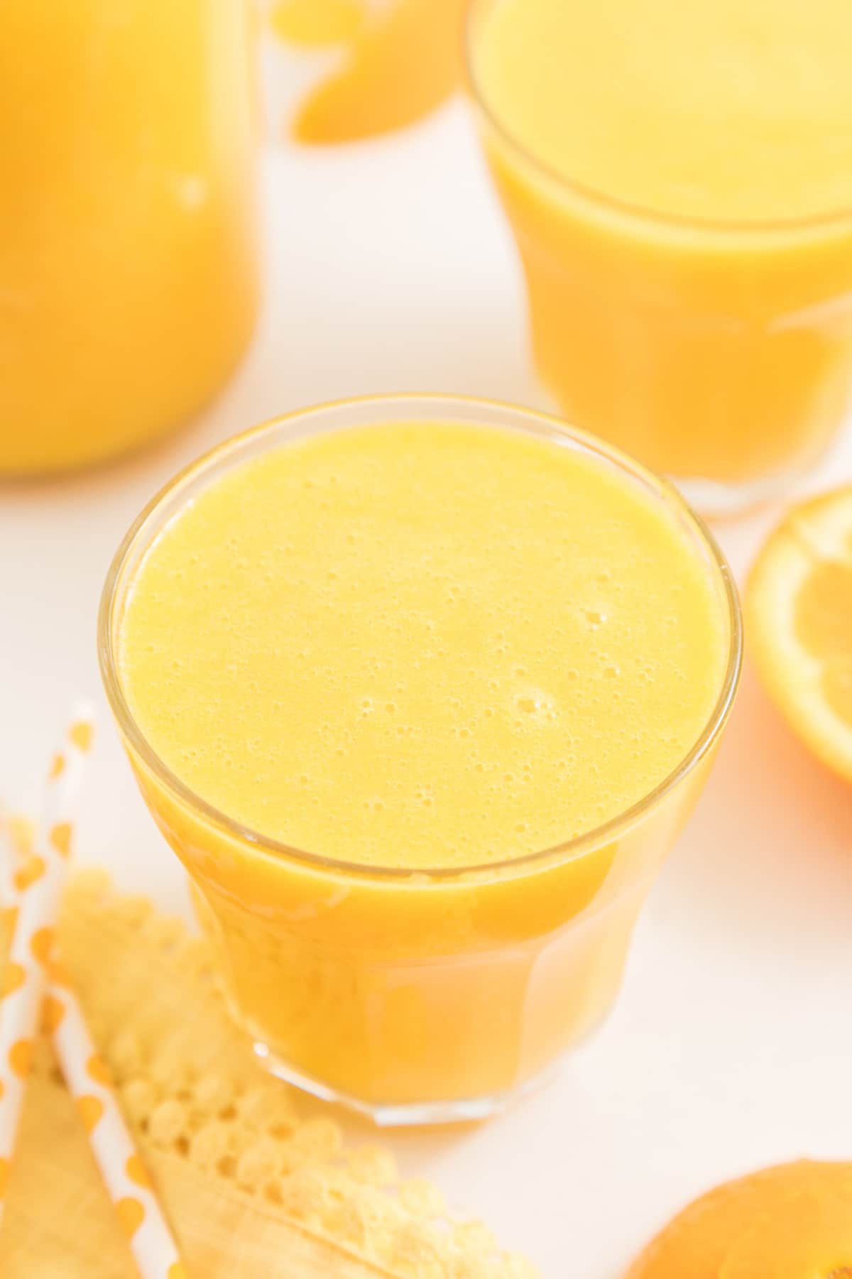blended orange juice served in low glass on table with fresh oranges.
