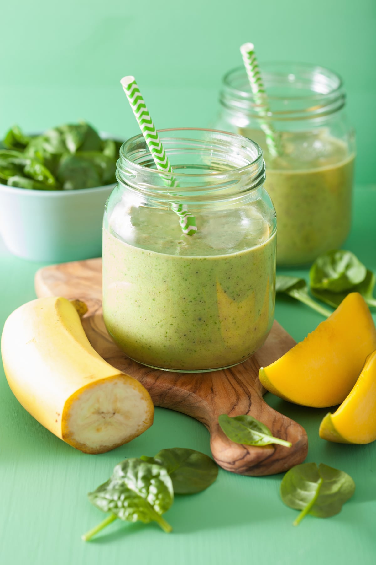 two weight loss green smoothies next to bananas, mango and spinach.