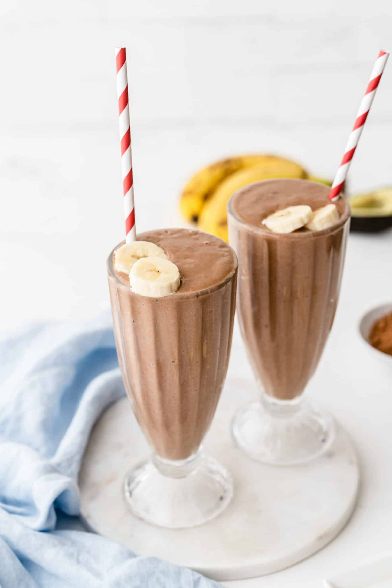 two glasses of avocado chocolate smoothie with straws.
