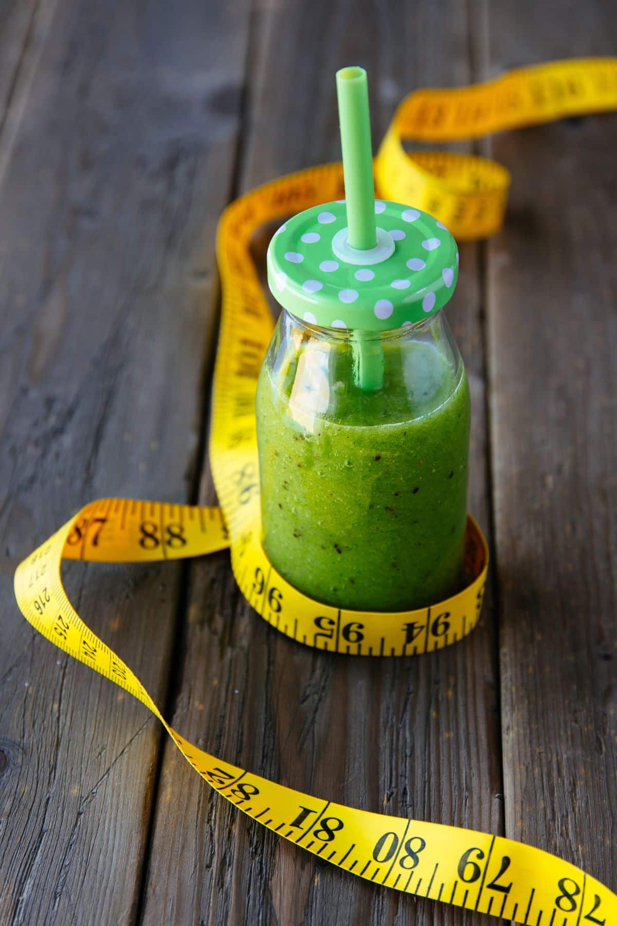 a green smoothie in a jar, surrounded by a measuring tape.