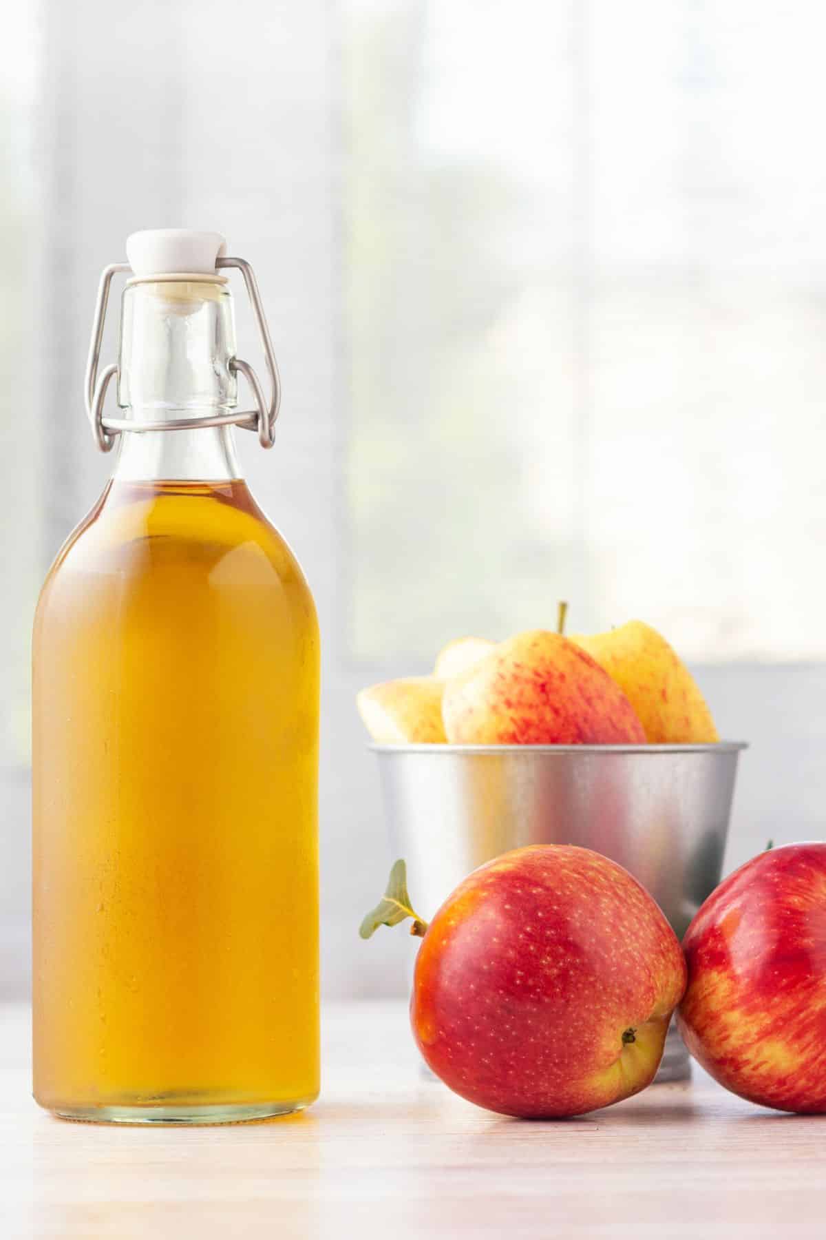 a bottle of apple cider vinegar next to red apples.