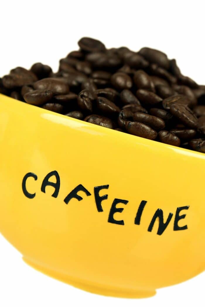 a yellow cup labeled "caffeine" full of coffee beans.