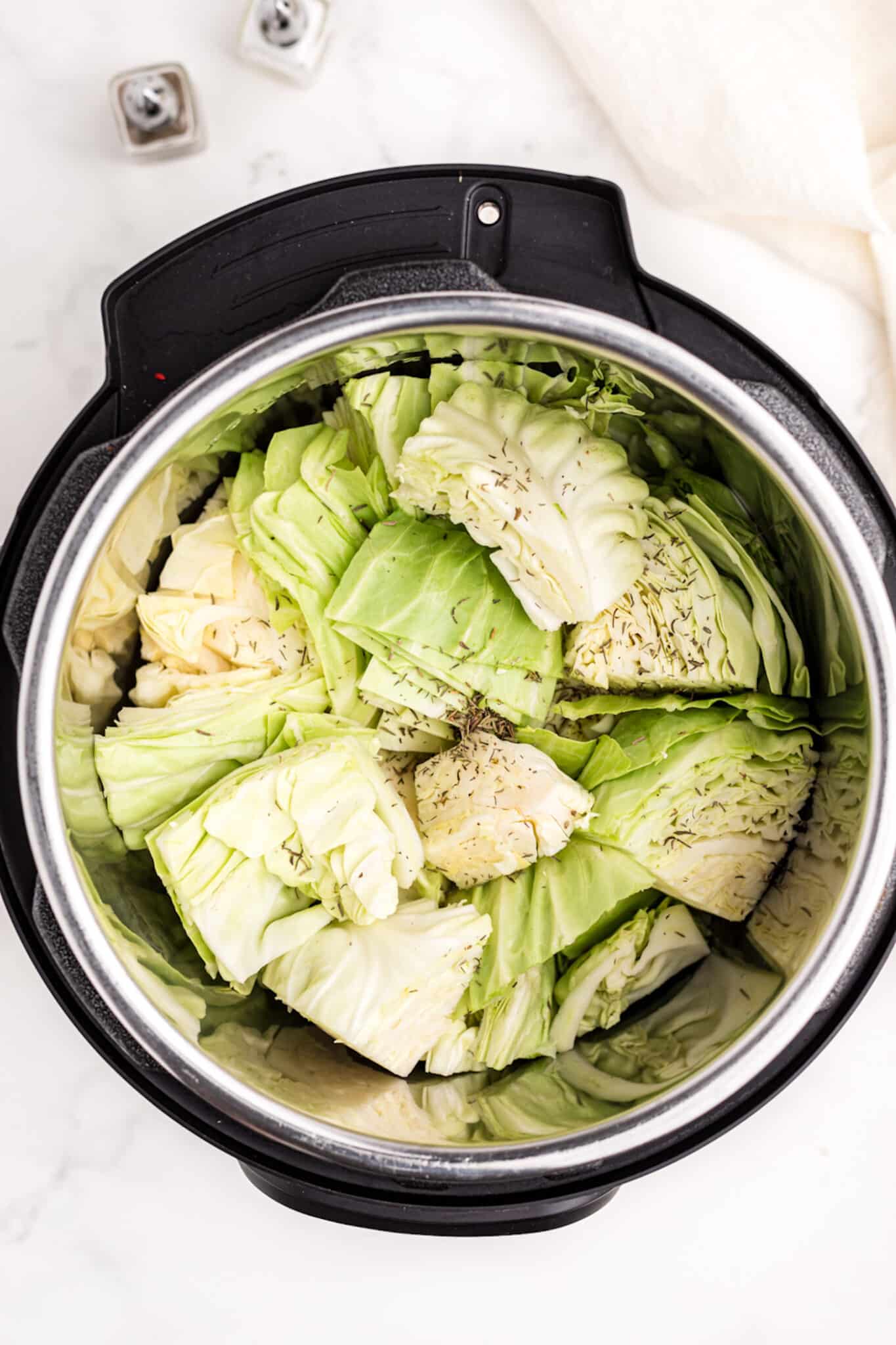 chopped cabbage inside instant pot with broth and dried herbs.