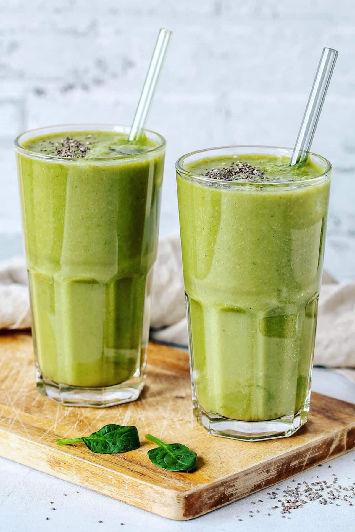 two glasses of green smoothie with straws.