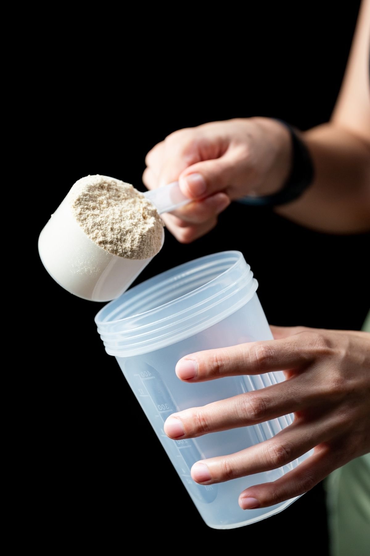 a person pouring whey protein into a shaker cup.