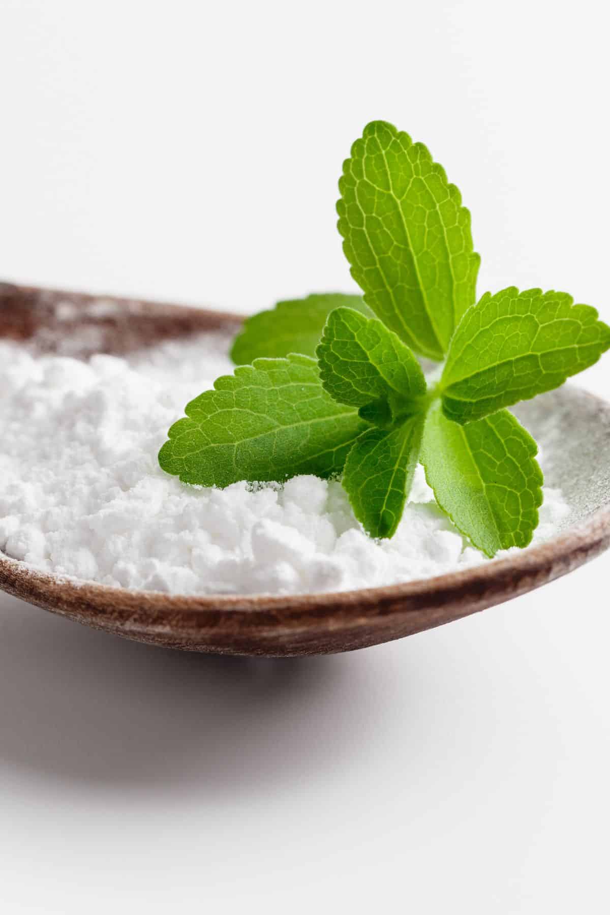 powdered stevia in a wooden spoon topped with a stevia leaf.