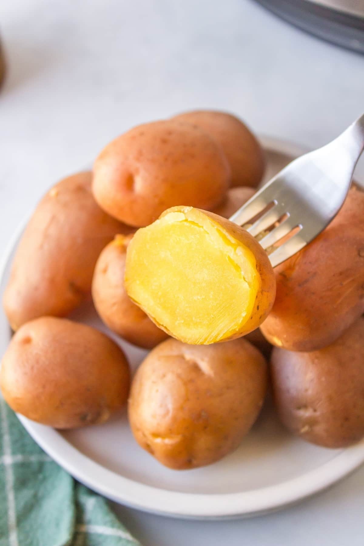 instant pot gold potato cut in half on a fork with other cooked potatoes.