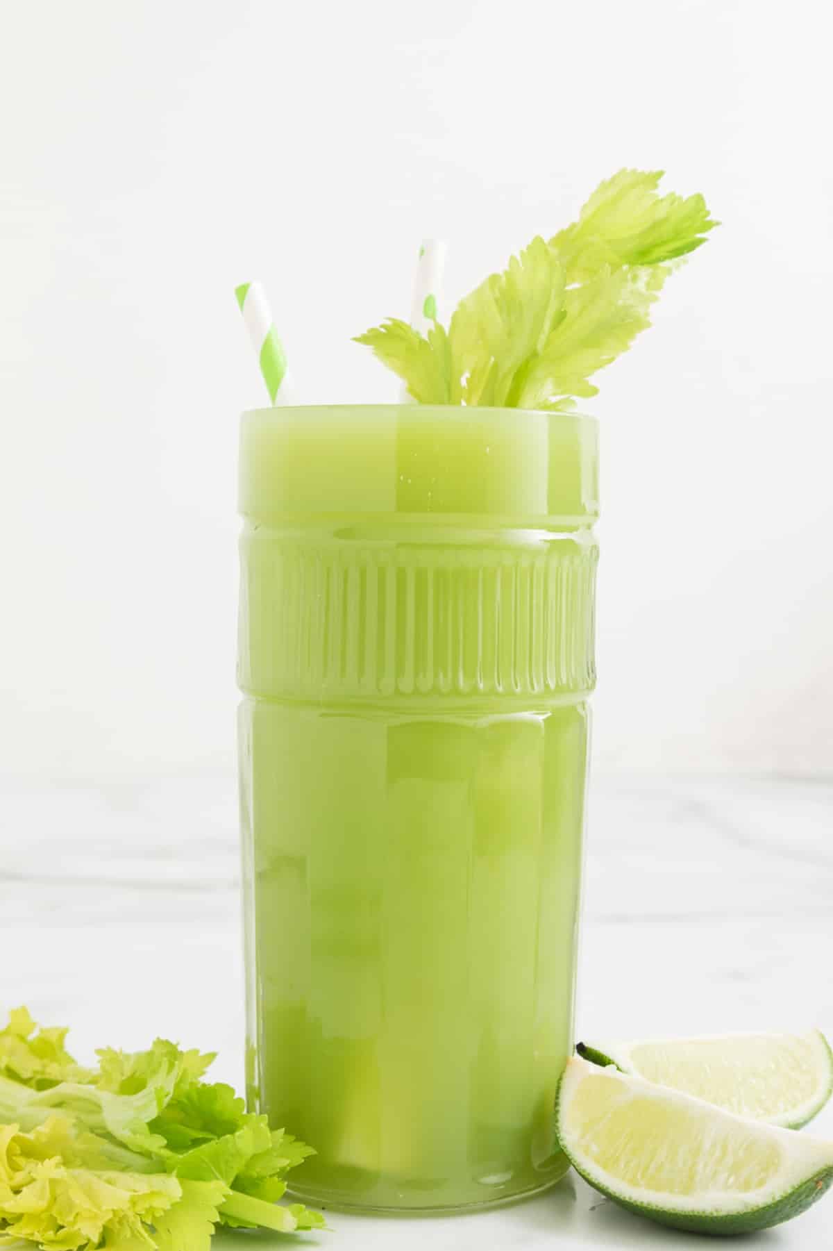 large glass of celery lime juice garnished with celery leaves.