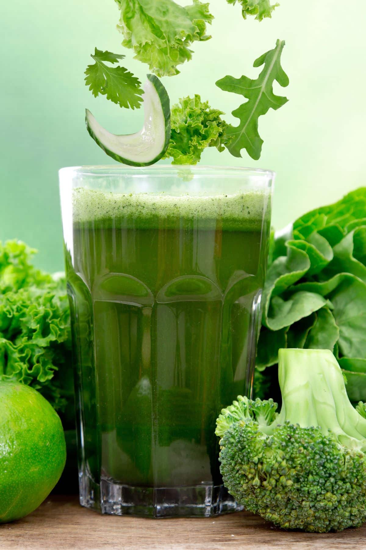a glass of green juice surrounded by vegetables.