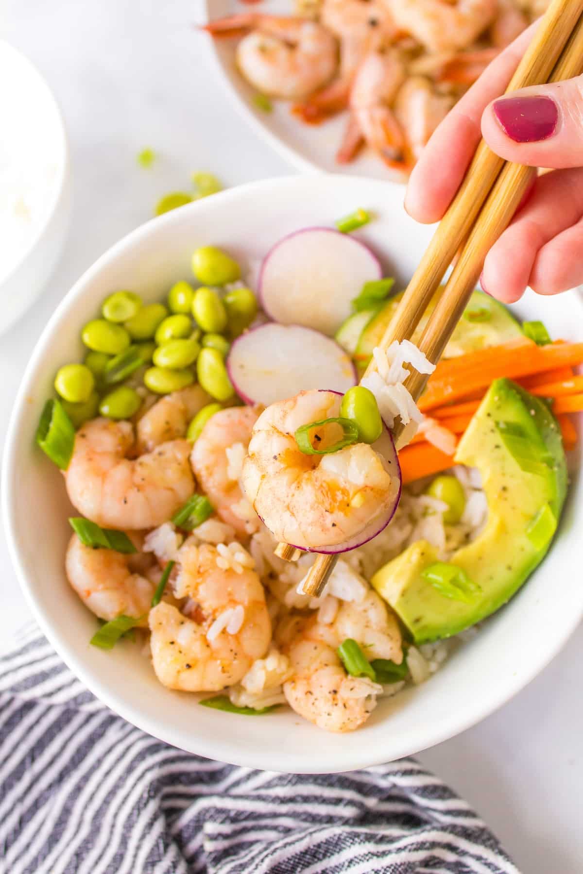 chop sticks holding a bite of a shrimp poke bowl.